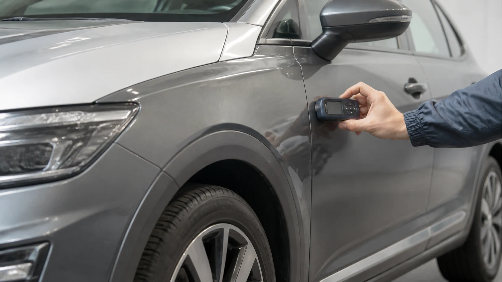 Handheld gauge beside different car panel materials during paint inspection